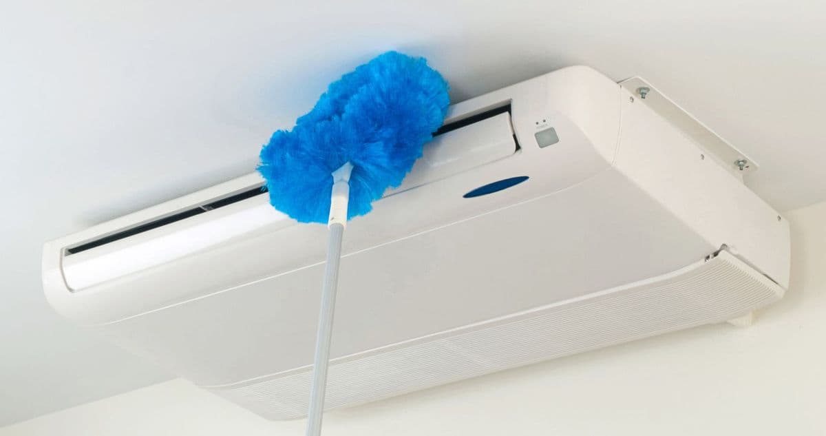 A blue electrostatic duster being used to clean an indoor air-conditioning unit