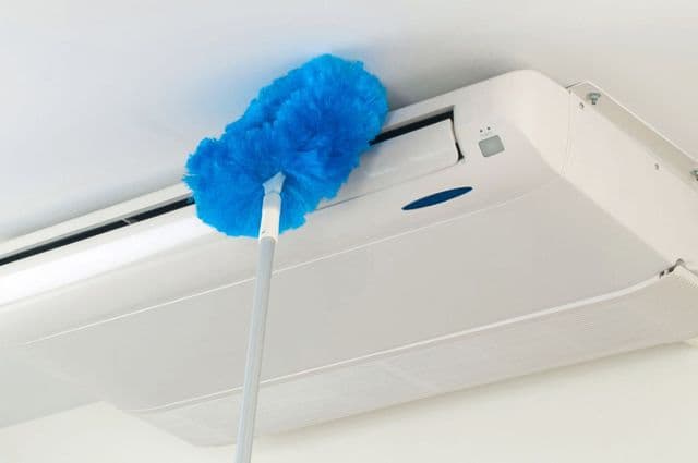 A blue electrostatic duster being used to clean an indoor air-conditioning unit