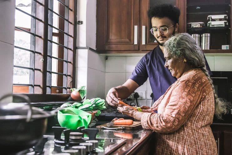 An adult man and older woman preparing food together in the kitchen