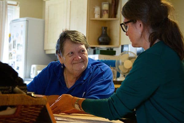 An adult woman assisting an older woman at a kitchen table