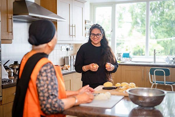 An adult woman helping an older woman prepare food in the kitchen