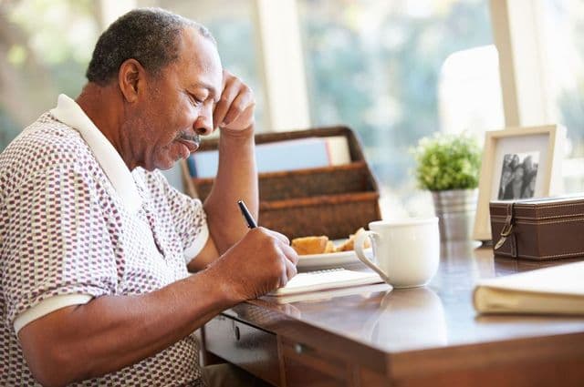 An older man sitting at a desk, writing in a notebook