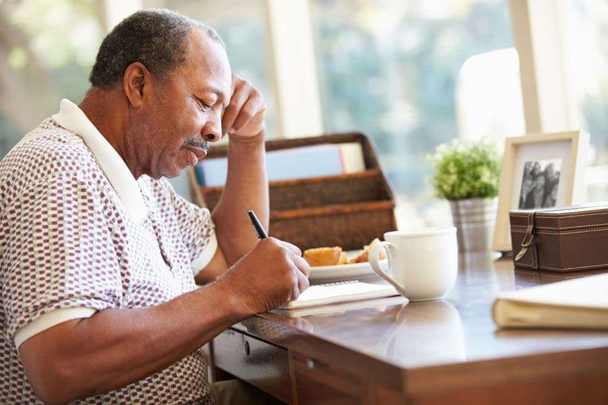 An older man sitting at a desk, writing in a notebook