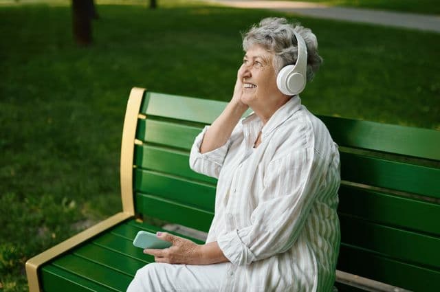 An older woman listening to her mobile phone using headphones