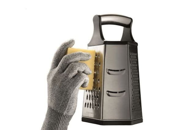 A hand in a silver cut-resistant glove grating cheese