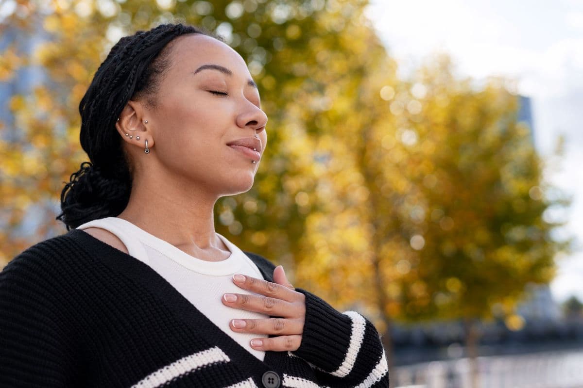 A young woman takes deep, calming breaths in a park.