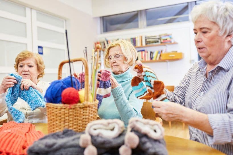 Three older women knitting together in a group