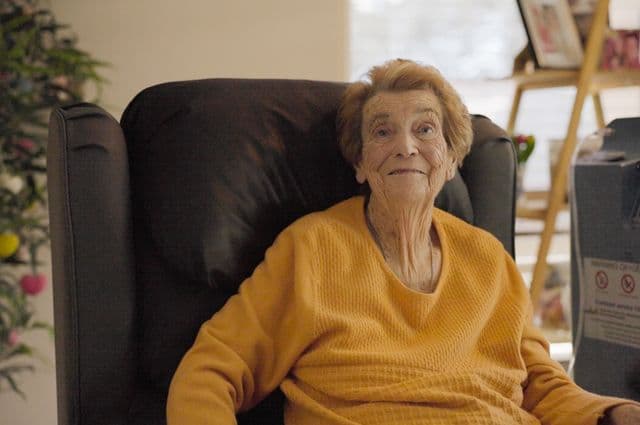 Older woman Jill sitting on her living room chair, smiling.
