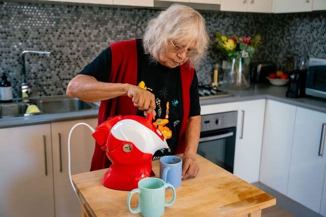 An older woman uses the kettle tipper to pour hot water for her tea.