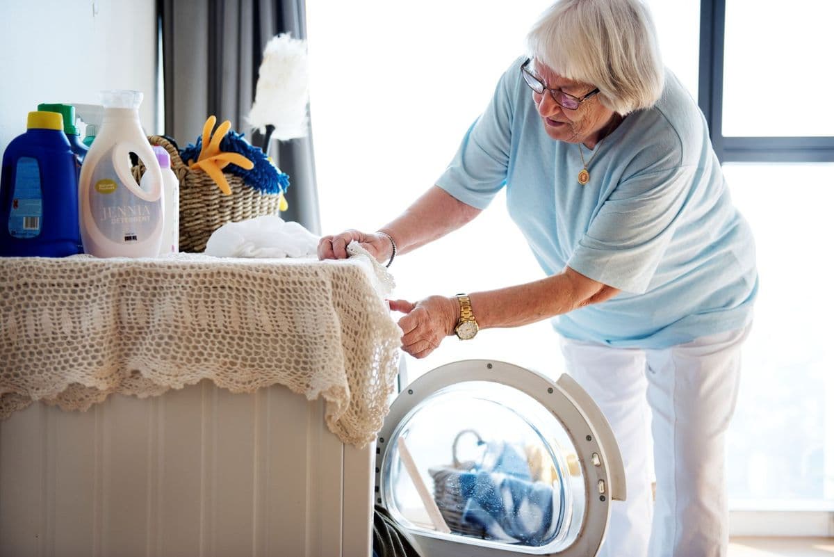 An older woman putting her laundry in the washing machine.