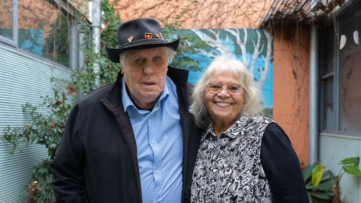 An older First Nations couple standing among greenery together