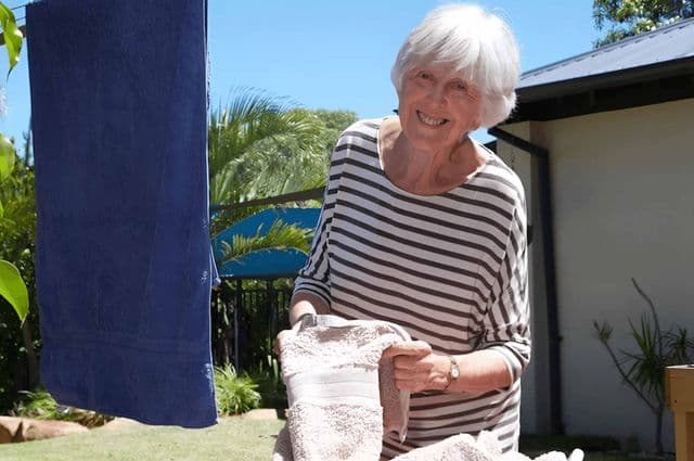Older woman smiling as she hangs out towels