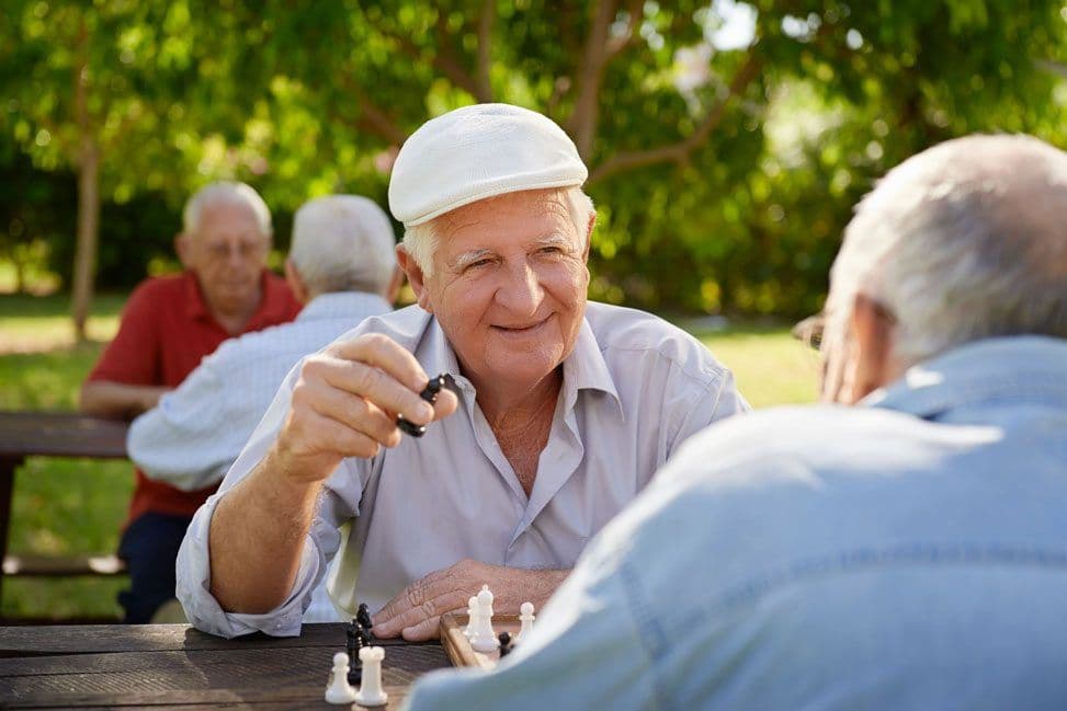 An older man happily playing chess with another man outside