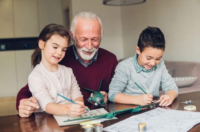 An older man constructing a miniature plane with his grandchildren