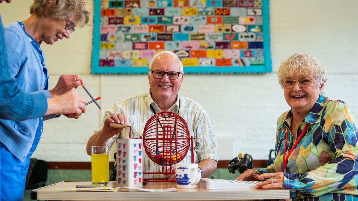 An older man spinning a bingo machine sitting in between two older women