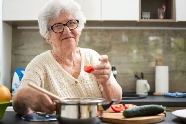 An older woman cooking with tomatoes.