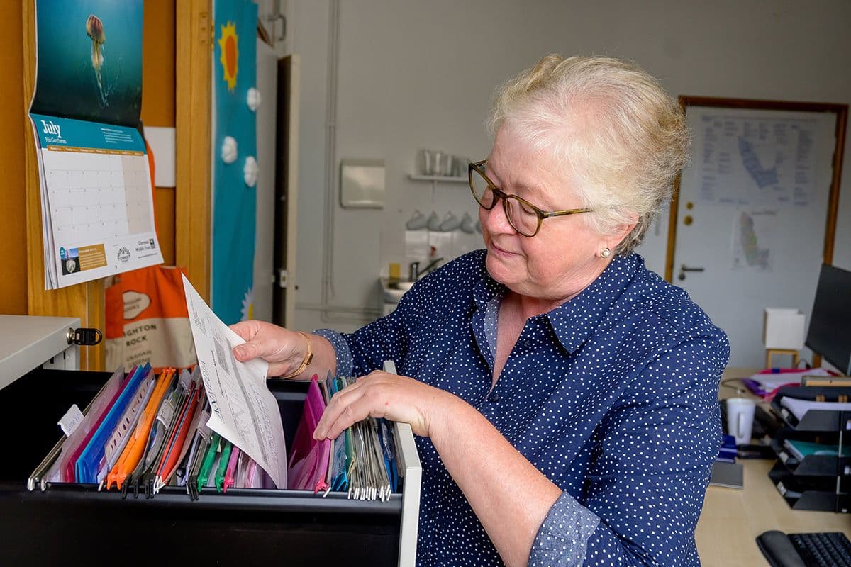 An older woman with short, light-coloured hair organising files in a drawer in an office