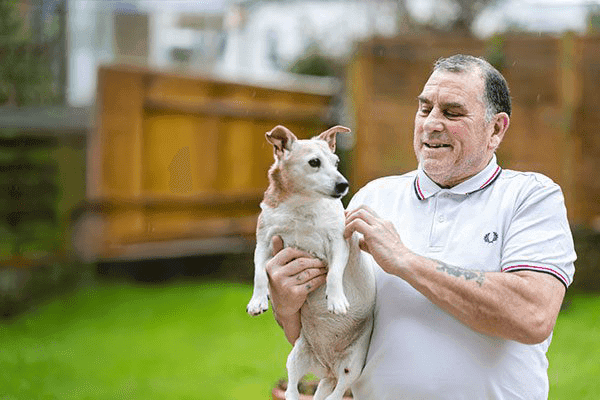 An older man holding and petting a small dog