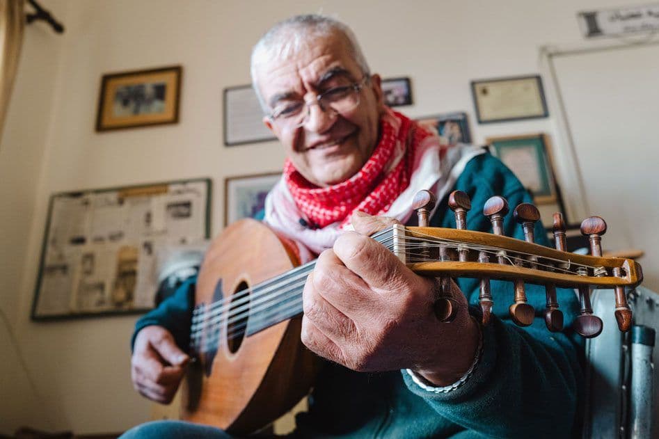 Older man happily playing a stringed instrument while seated inside
