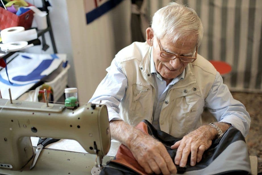 Older man happily using a sewing machine on a piece of clothing