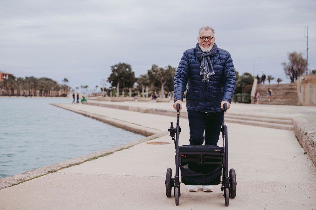 Older man happily walking by a lake using a walker