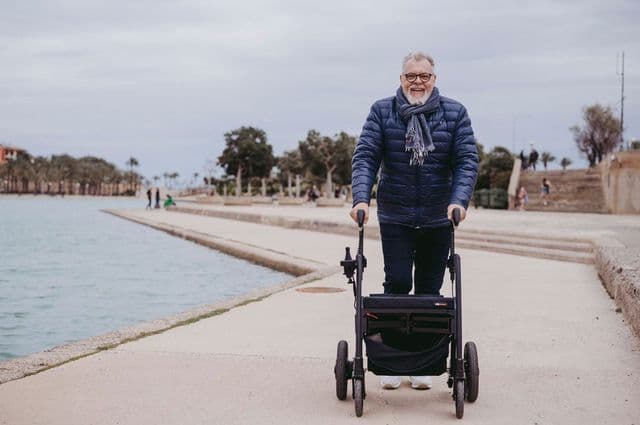 Older man happily walking by a lake using a walker
