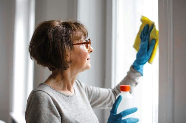 An older woman wiping a window with a cleaning cloth