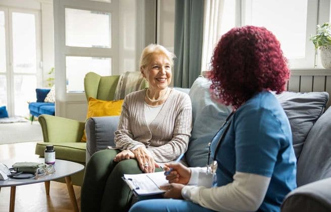 An older woman and adult woman in nursing scrubs happily completing a checklist together