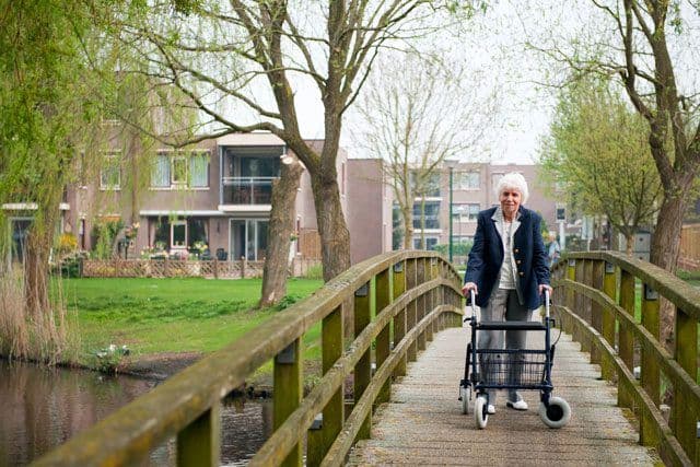An older woman using a walker to walk across a bridge