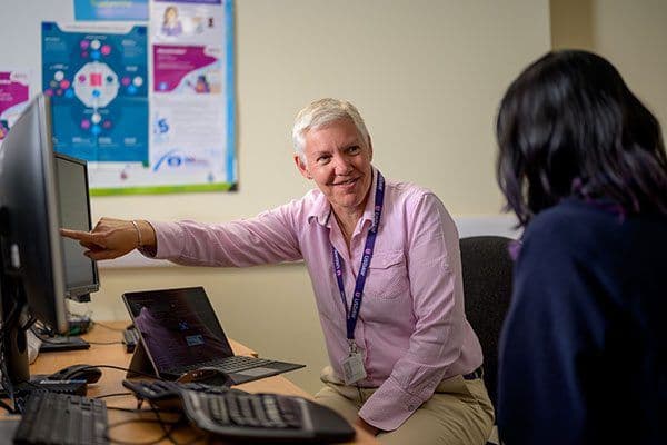 A short-haired woman pointing at a computer screen while speaking to another woman