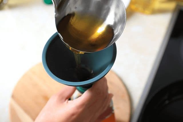 A person using a silicone funnel to pour liquid into a bottle