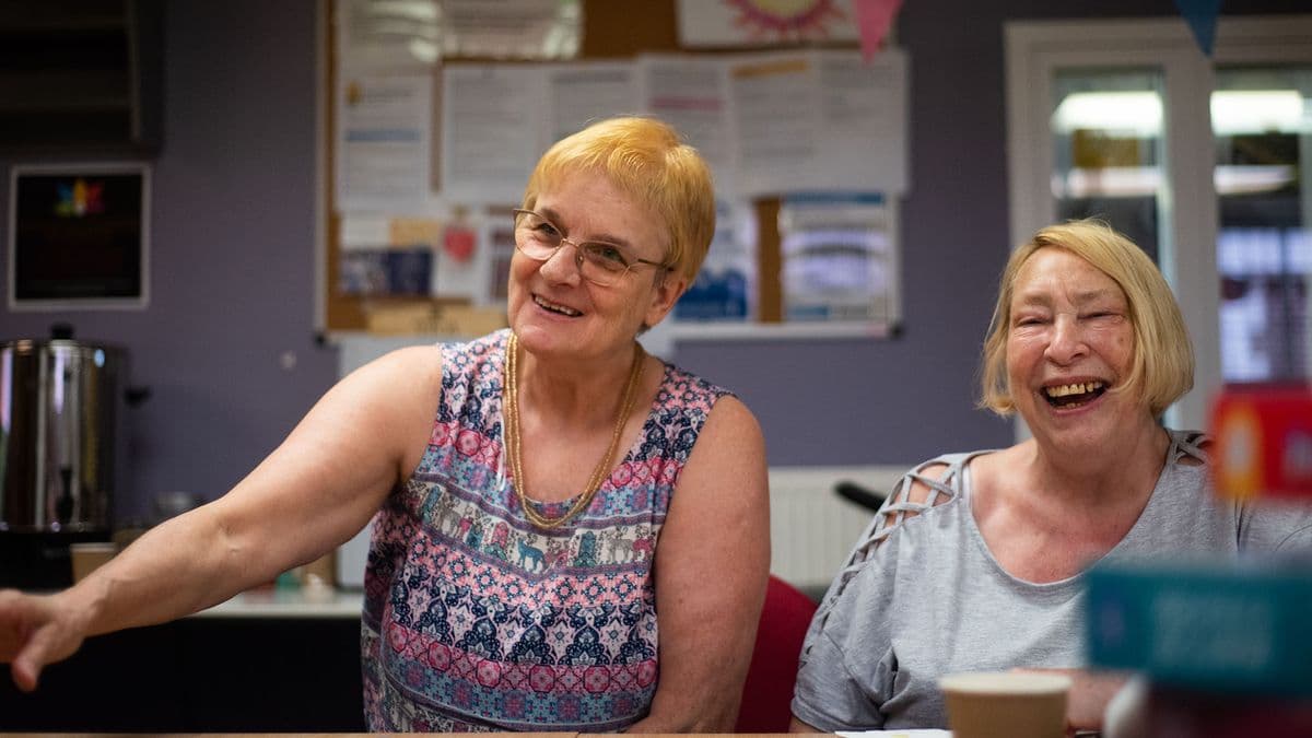 Two older women laughing at a table together