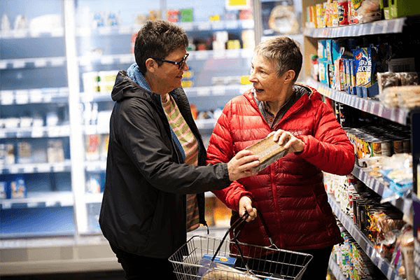 Two women with short hair shopping for food items at a grocery store