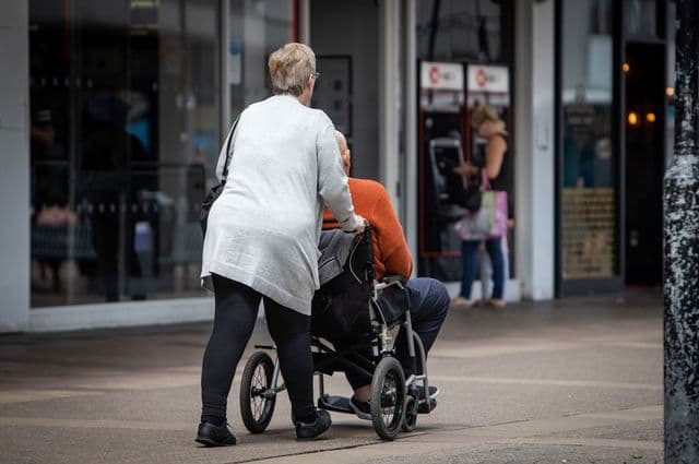 An older woman pushing the wheelchair of an older man.