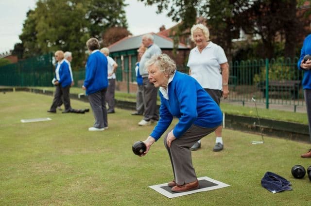 An older woman bending down to roll a lawn bowl
