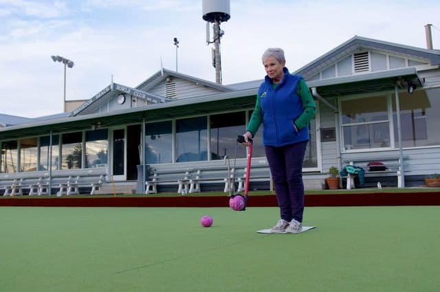 A woman on a bowling green using a bowling arm