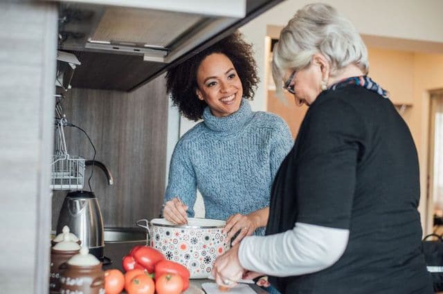 An older woman preparing food in the kitchen with a younger counterpart