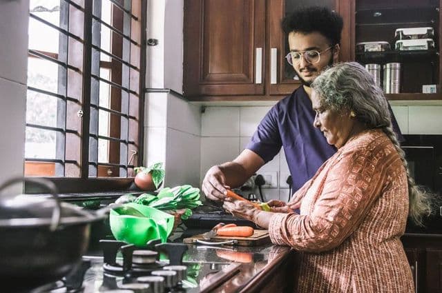 An adult man and older woman preparing food together in the kitchen