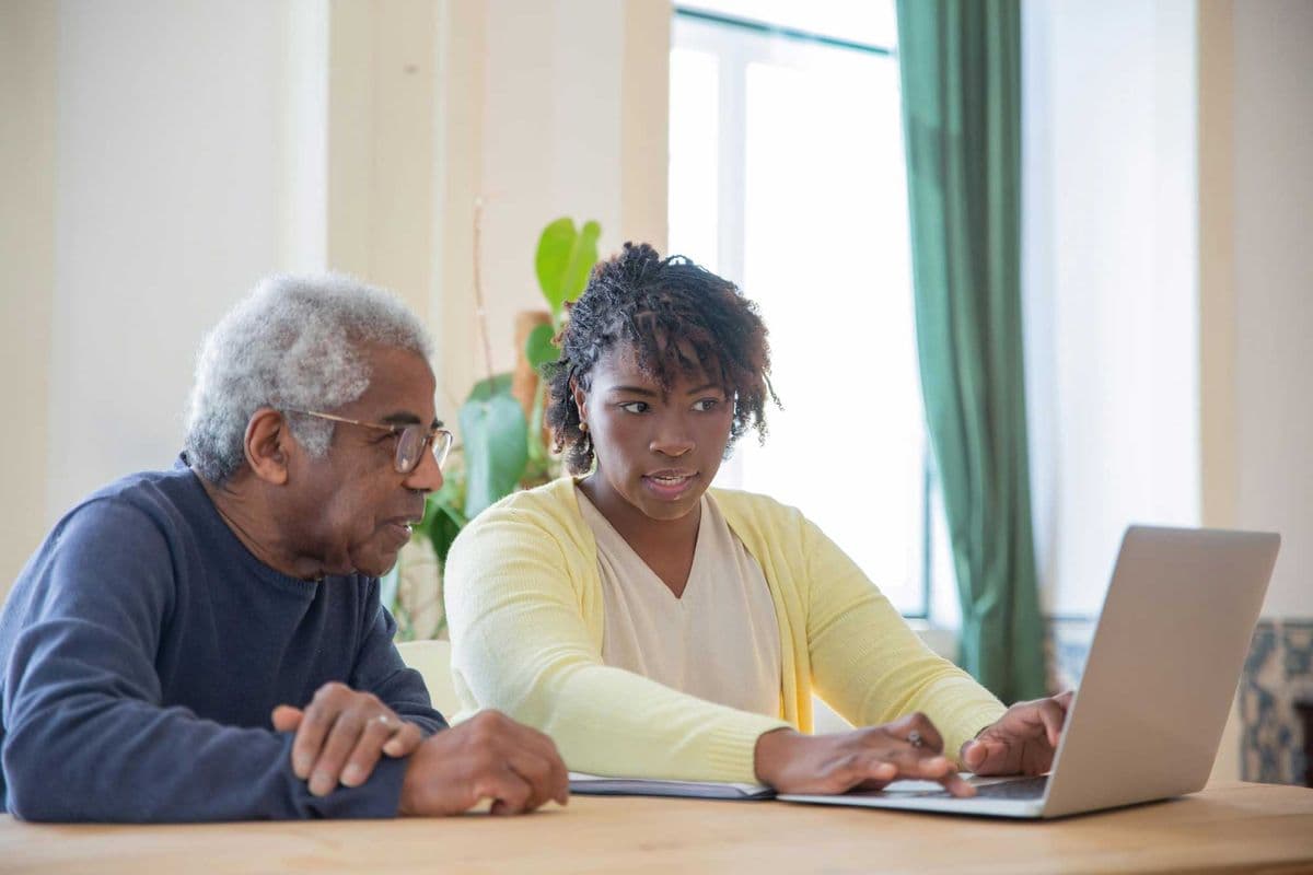 Older man sitting next to his support worker while she uses a laptop