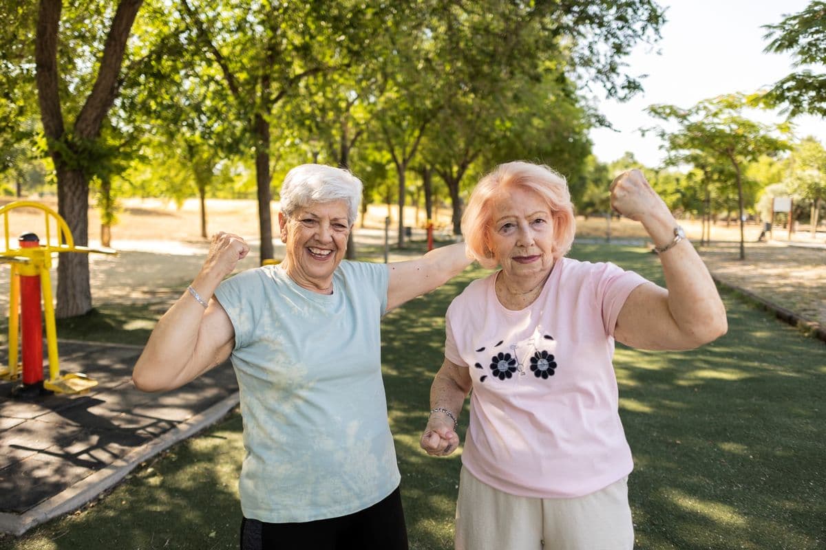 Two older women showing off strong arms in the park.