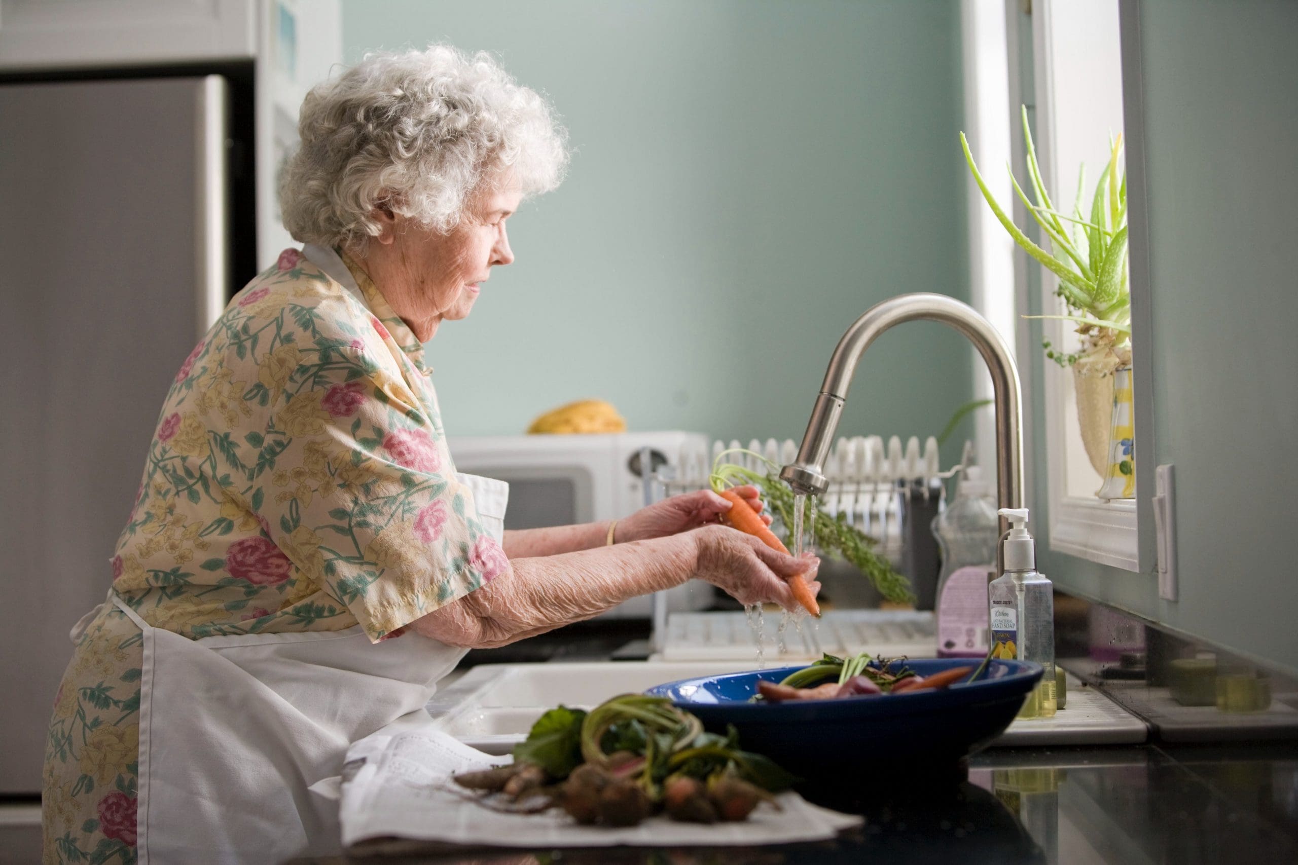 Older lady washing vegetables under a tap preparing a meal