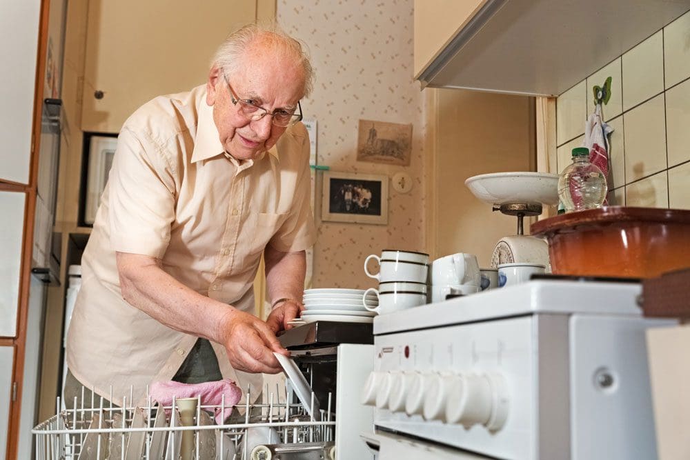 Elderly man loading a dishwasher