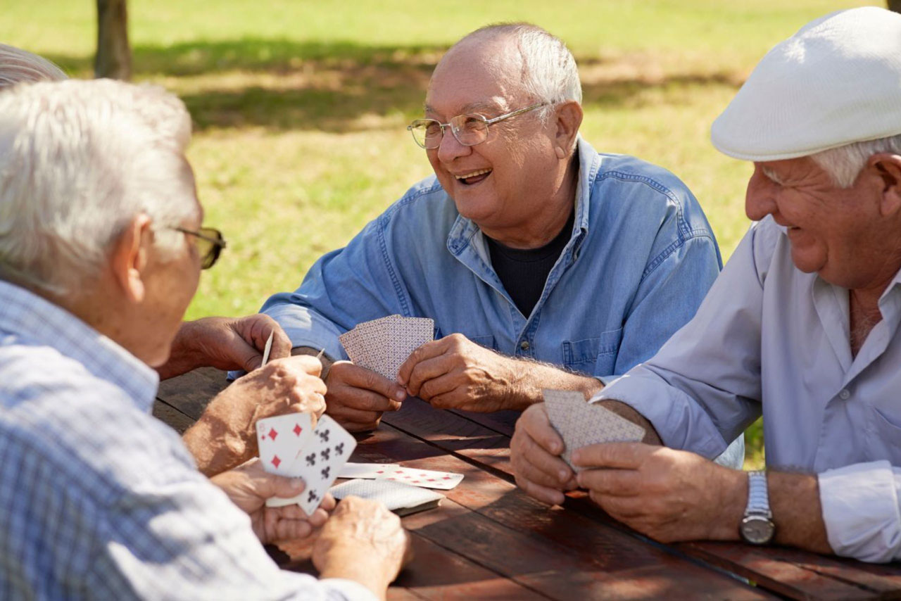 A group of older men happily playing card games in the sunshine