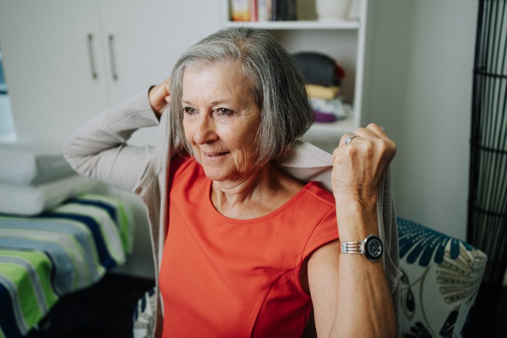 Older lady putting a cardigan on